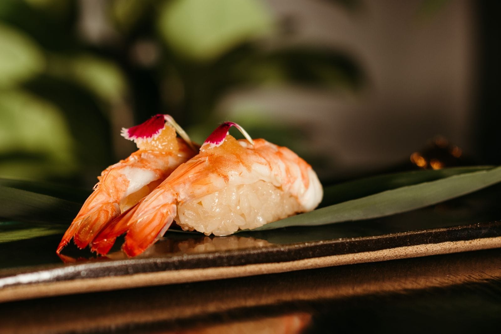 Shrimp nigiri garnished on a dark plate