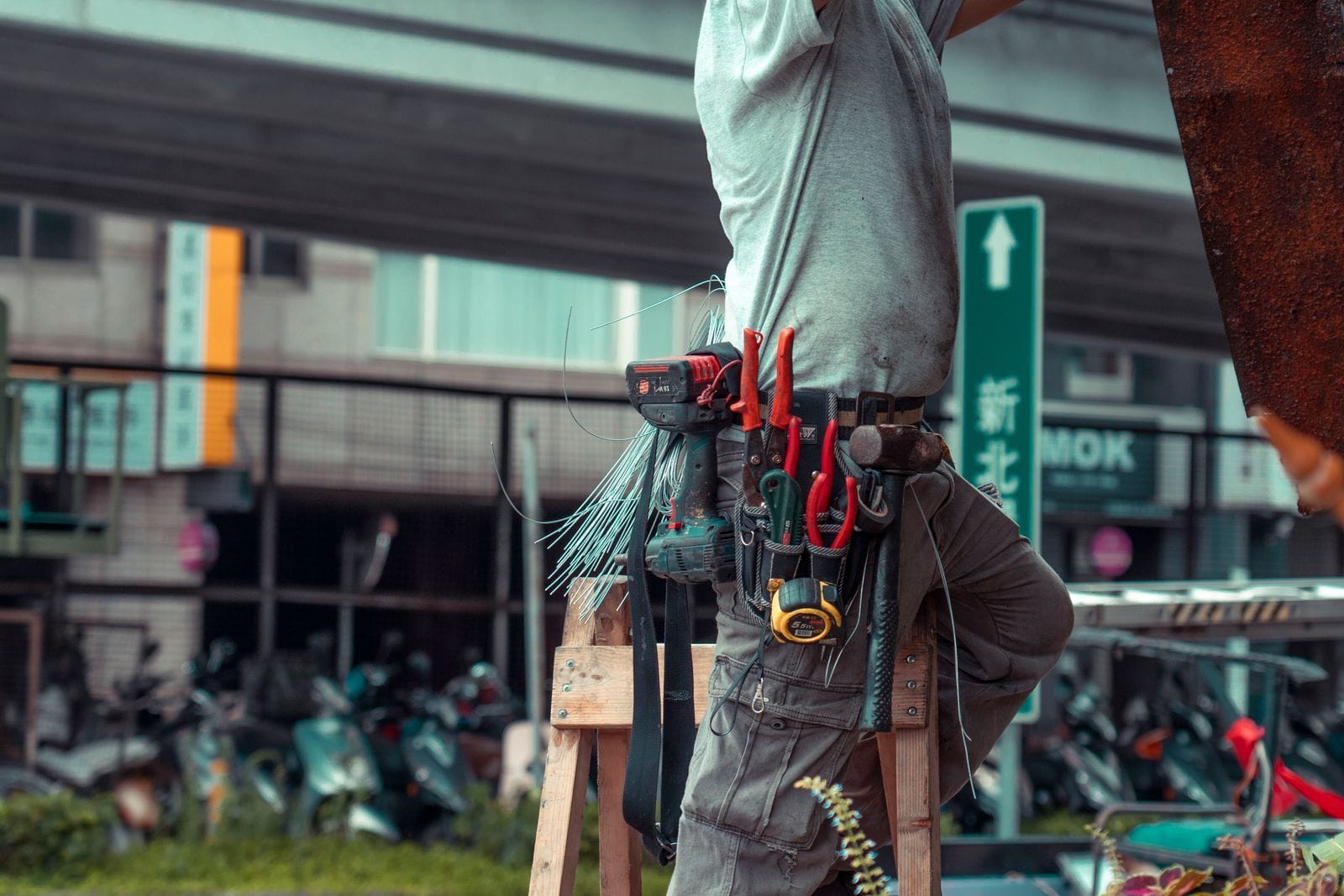 Handyman standing on a ladder with a tool belt while working outdoors