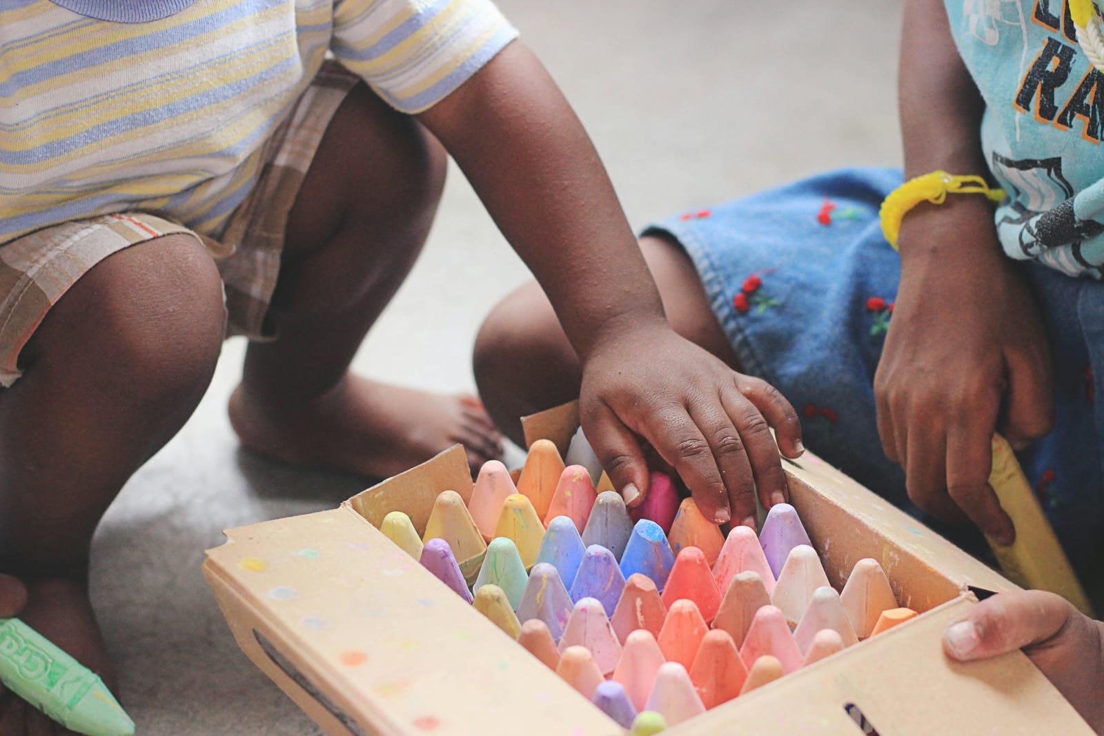 Brown children reaching into a box of colorful play materials